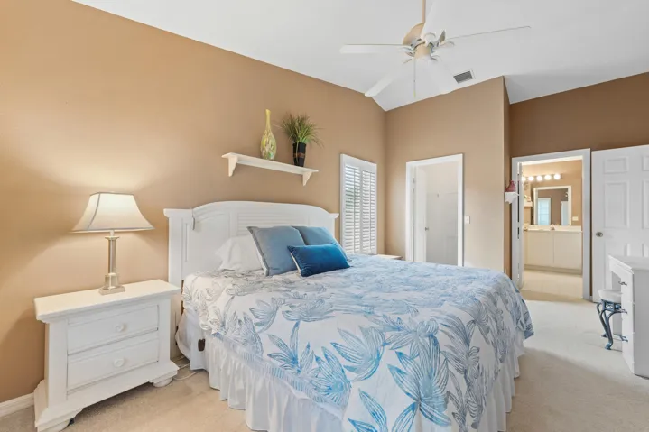 Vaulted ceiling with a white overhead fan, wall-mounted display shelf, carpeted flooring, and white plantation shutters
