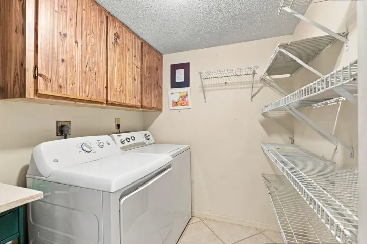 Wood-finish upper cabinetry provides storage above a laundry area with tile flooring and wire shelving