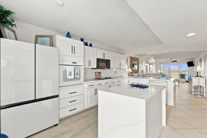 White cabinetry with dark hardware, built-in oven, integrated microwave, and a center island with a waterfall countertop