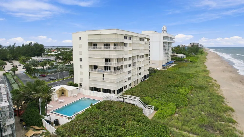 Multi-story condominium building featuring private balconies, a swimming pool, and direct beach access