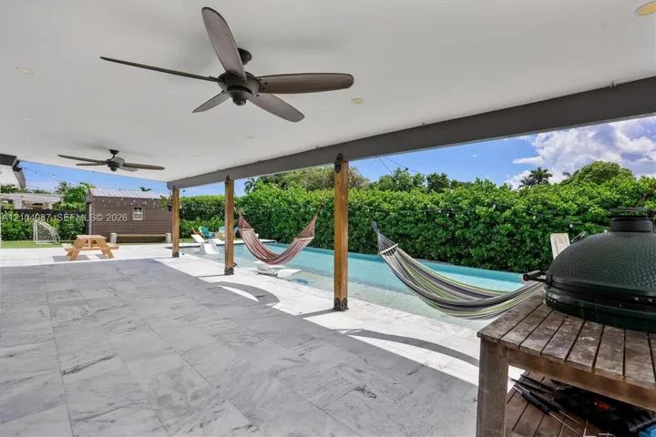 Covered patio with integrated ceiling fans, a full-length swimming pool, and a stone tile outdoor surface