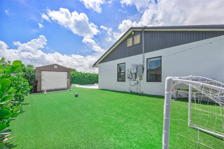 Expansive backyard featuring artificial turf, mature hedges, and a detached storage shed