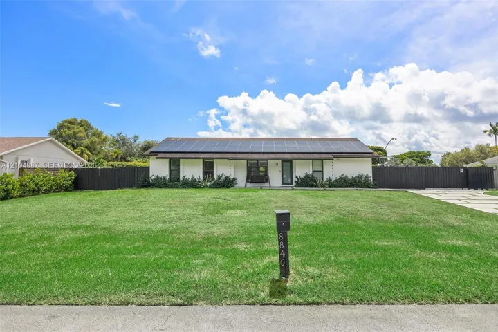 White exterior with dark trim accents, solar panel array, black fence, and a paver driveway