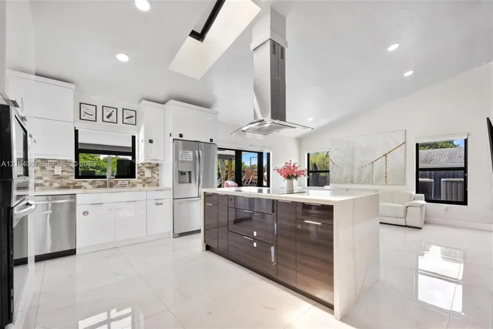 Modern kitchen featuring white cabinetry, stainless steel appliances, a center island with a wood-finish base, and vaulted ceilings with a skylight