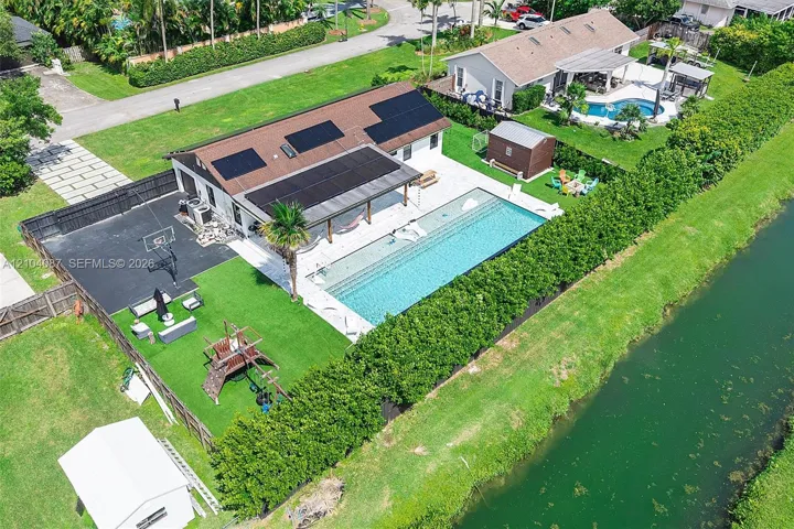 Exterior featuring a large in-ground swimming pool, covered patio, sport court, and artificial turf lawn
