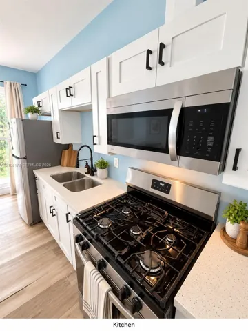 Kitchen featuring white shaker-style cabinetry with matte black hardware, stainless steel gas range and microwave, light-toned stone-finish countertops, and wood-finish flooring