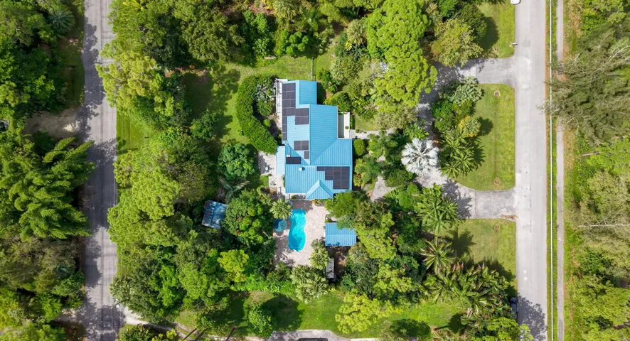 Aerial perspective featuring a property with a vibrant blue roof, integrated solar panels, and a freeform swimming pool