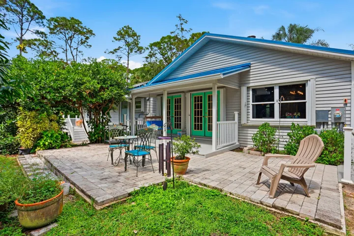 Expansive paver patio with a white railing porch, double-pane windows, and light green French doors