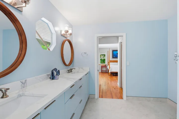 Dual vanity with integrated sinks and white countertops, light blue cabinetry, and a circular wooden-framed mirror