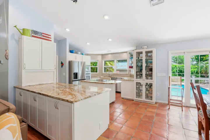 Kitchen featuring dual islands with stone countertops, white cabinetry, integrated stainless steel appliances, and terra cotta tile flooring