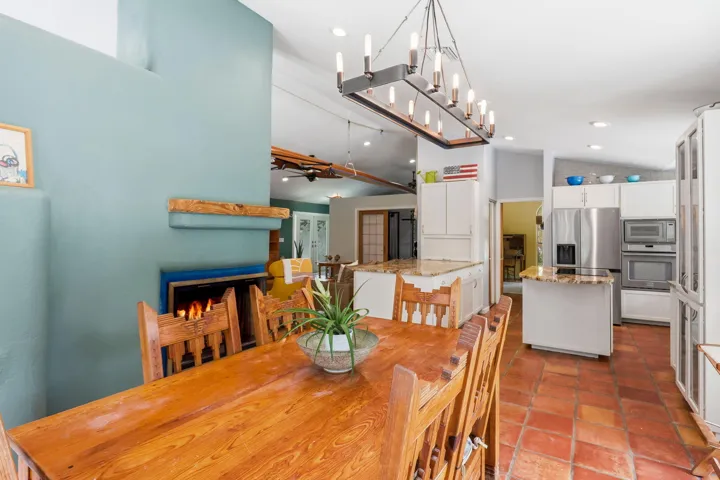 Kitchen and dining area featuring a fireplace, terracotta tile flooring, white cabinetry, stainless steel appliances, and granite countertops