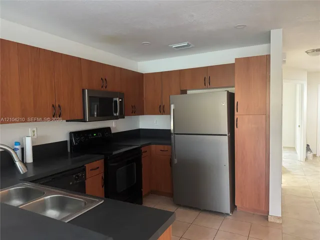 Kitchen featuring wood-finish cabinetry, black countertops, stainless steel refrigerator, stainless steel microwave, and black electric range