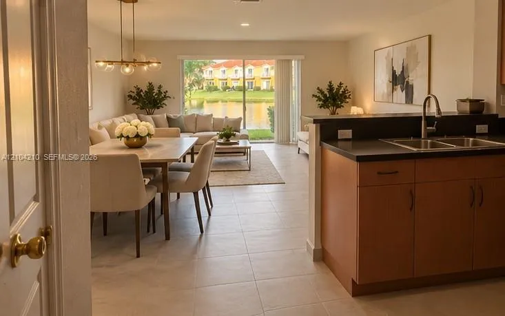 Open concept living space featuring tile flooring throughout, a dining area with a modern chandelier, and a kitchen with wood-finish cabinetry and a double basin sink