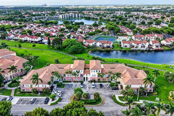 Aerial view of a multi-unit complex featuring clay-tile roofing, stucco exterior, paved parking areas, and mature palm tree landscaping