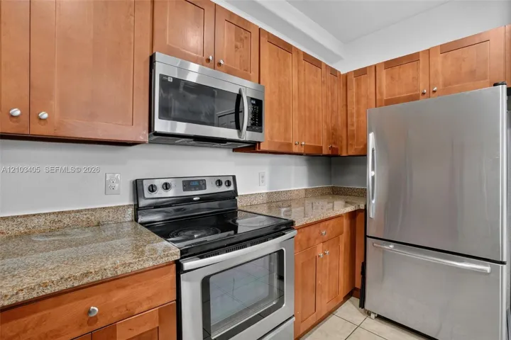 Kitchen featuring natural wood cabinetry, stone-finish countertops, and stainless steel appliances including a built-in microwave and refrigerator