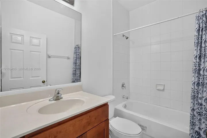 Bathroom featuring a vanity with a light-toned countertop, an integrated sink, a full-width mirror, and a shower-tub combination with white wall tile