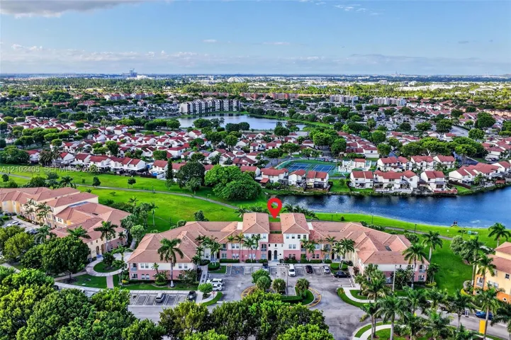 Aerial perspective of multi-unit residential complex featuring terracotta tile roofing, stucco exterior, surface parking, and extensive waterfront landscaping