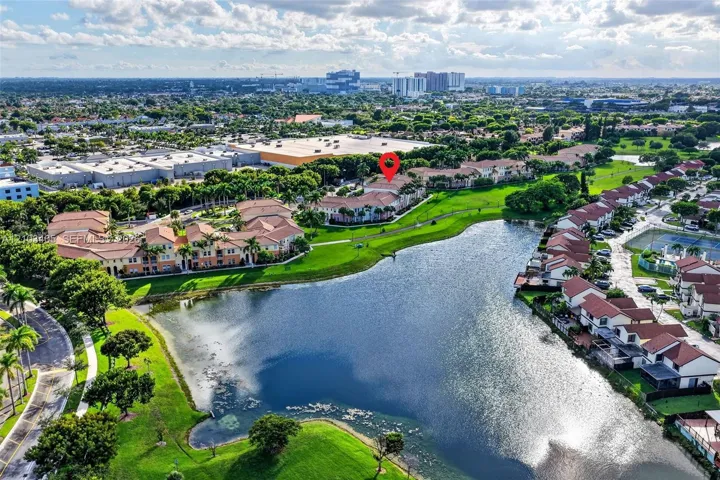 Aerial perspective featuring a multi-building residential community with red tile roofing, situated along a central lakefront with surrounding green space and mature landscaping