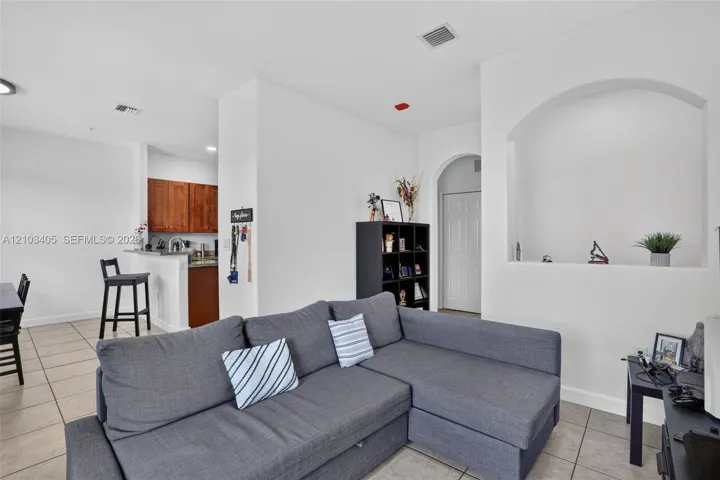 Open-concept interior featuring large-format tile flooring, a built-in recessed wall niche, arched architectural detailing, and a kitchen pass-through counter with dark wood-finish cabinetry