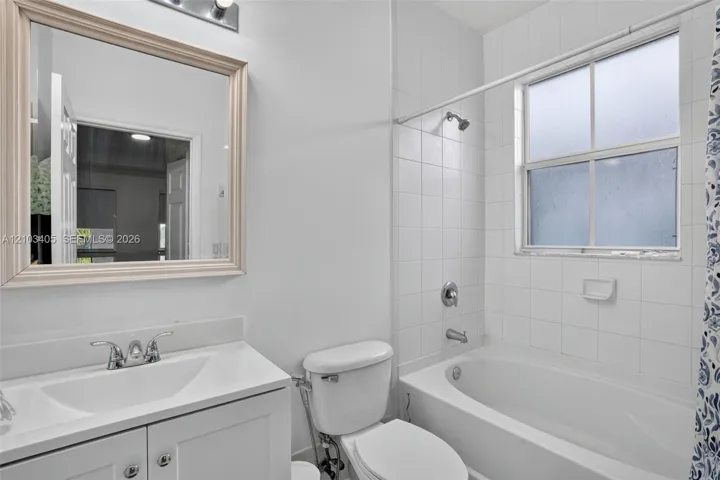 Bathroom featuring a white vanity with integrated sink, framed vanity mirror, chrome finish fixtures, and a shower-tub combination with white tile surround