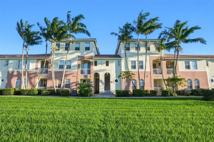 Multi-story stucco exterior featuring arched entryways, private balconies, clay tile roofing, and mature palm landscaping