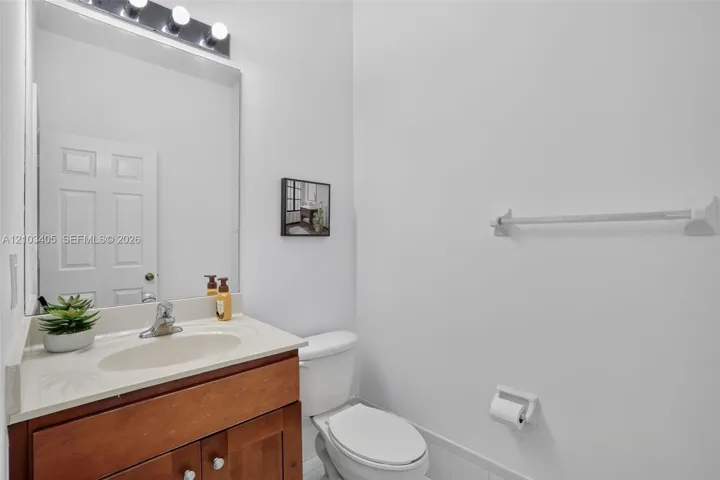 Wood-finish vanity cabinet, integrated countertop basin, chrome-finish faucet, and full-width mirror with overhead multi-bulb lighting