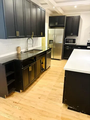 Kitchen featuring matte black cabinetry with gold-tone hardware, wood-finish flooring, quartz countertops, a stainless steel undermount sink with a pull-down faucet, and a coffered ceiling