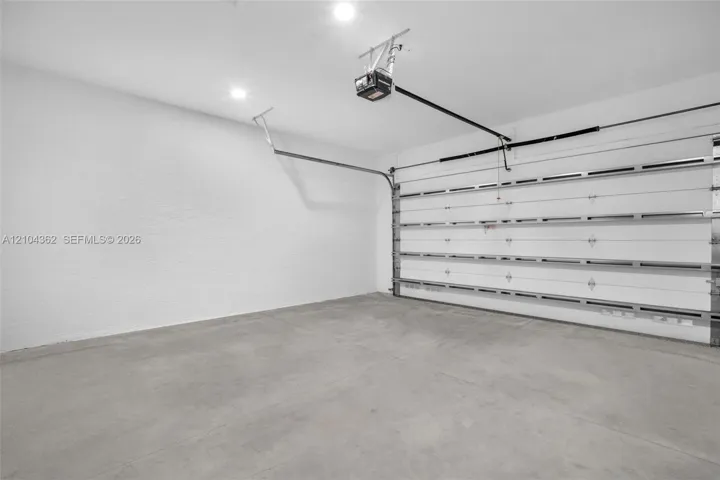 Garage interior featuring a concrete floor, finished white walls, recessed ceiling lighting, and a motorized garage door opener