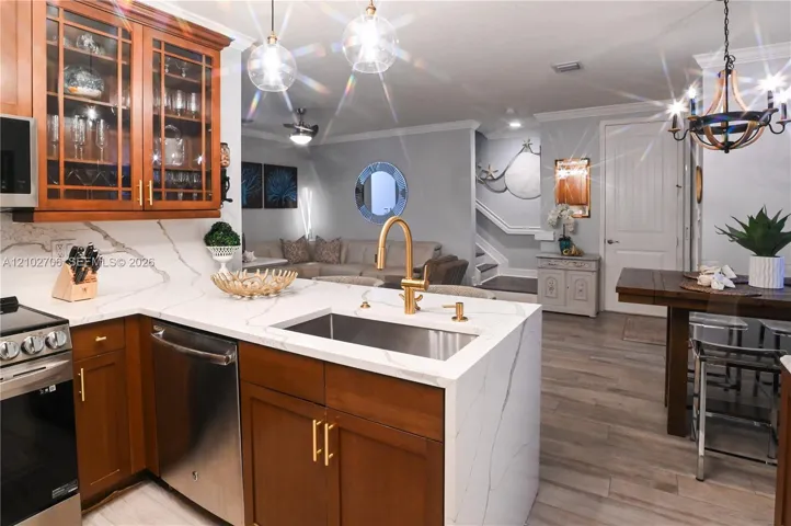 Kitchen featuring wood cabinetry, stone-finish countertops with waterfall edge, stainless steel undermount sink, brass-finish faucet, and wood-finish flooring