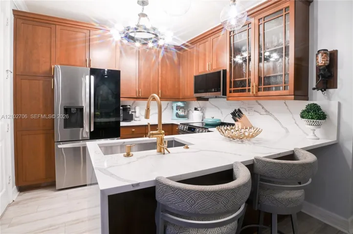 Kitchen featuring wood cabinetry, stone-surface countertops, stainless steel appliances, a brass-finish faucet, and overhead statement lighting