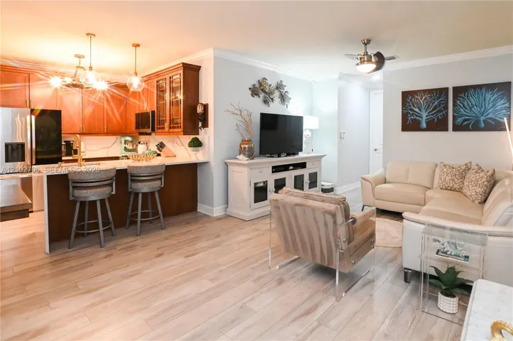 Open-concept interior featuring wood-finish flooring, a kitchen island with quartz countertops, custom cabinetry with glass-panel accents, crown molding, and a ceiling fan with integrated lighting