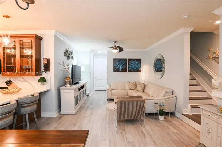 Open-concept interior featuring wood-finish flooring, crown molding, kitchen cabinetry with glass-panel doors, stone-patterned countertops, and a staircase with a white handrail