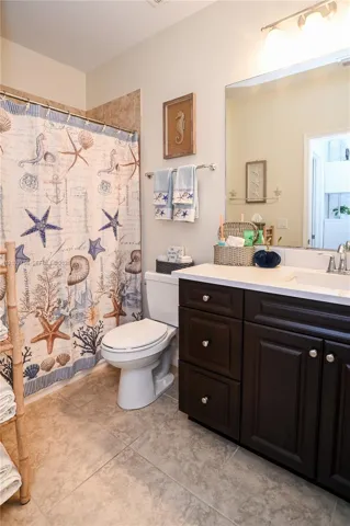 Dark-finish cabinetry, solid-surface countertop with an integrated basin, large-format tile flooring, and a full-width vanity mirror