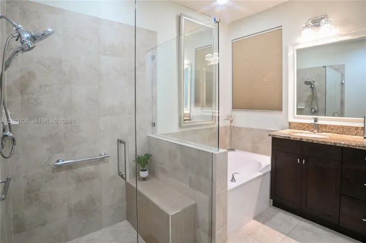 Walk-in tiled shower with a built-in bench, glass enclosure, soaking tub, dark wood-finish cabinetry, and vanity with an integrated sink