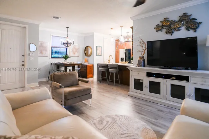 Open-concept interior featuring light wood-finish flooring, crown molding, a kitchen island with pendant lighting, and a neutral color​​‌​​​​‌​​‌‌​‌‌​​​‌‌​‌​‌​‌​​​‌​​ palette