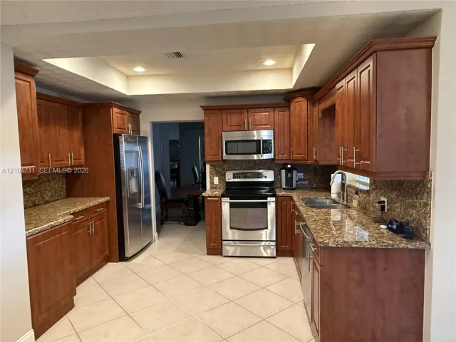 Expansive kitchen featuring wood-finish cabinetry, stainless steel appliances, granite countertops, and tile flooring