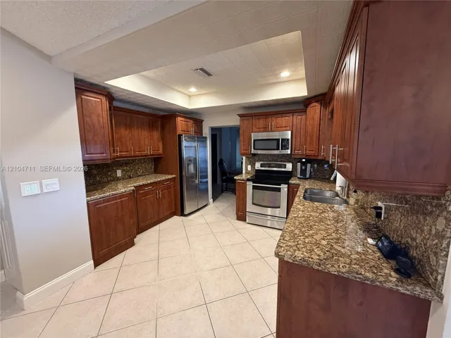 Kitchen featuring wood cabinetry, stainless steel appliances, granite countertops, and tiled flooring