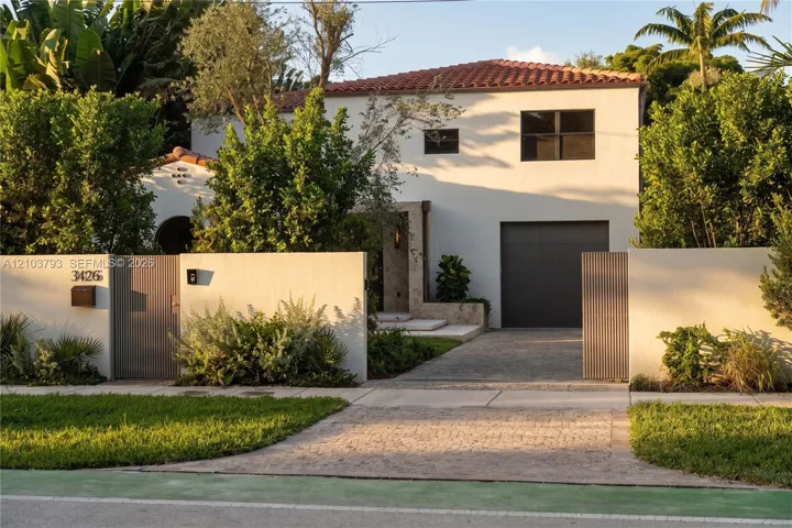 Two-story exterior featuring a smooth stucco finish, clay tile roof, stone-clad entrance, vertical slat privacy gates, and a paved stone driveway