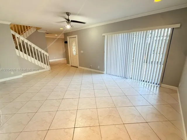 Open-concept interior featuring large-format ceramic tile flooring, staircase with white railing, sliding glass doors with vertical blinds, and a ceiling fan