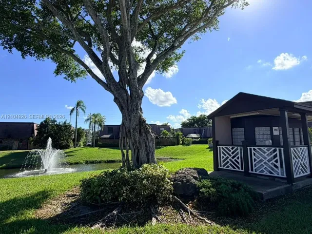 Community grounds featuring a water fountain, mature tree, manicured lawn, and covered mail kiosk with decorative lattice railing