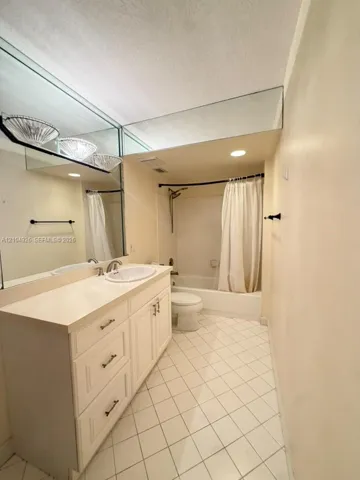Bathroom featuring a white vanity cabinet, solid-surface countertop with an integrated basin, expansive wall-to-wall mirror, and neutral tile flooring laid on a diagonal