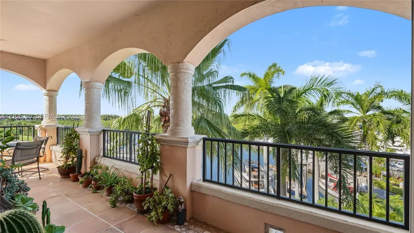 Covered terrace featuring arched architectural detailing, textured stone columns, tile flooring, and a metal railing