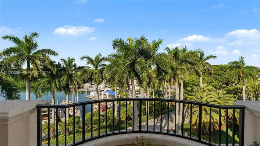 Curved balcony featuring a black metal railing, concrete-finish parapet, and water-facing orientation overlooking mature palm trees and a marina