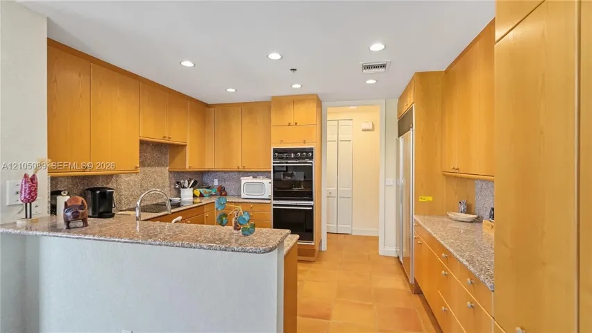 Kitchen featuring light wood cabinetry, stone-surface countertops, built-in double wall oven, integrated refrigerator, and recessed lighting