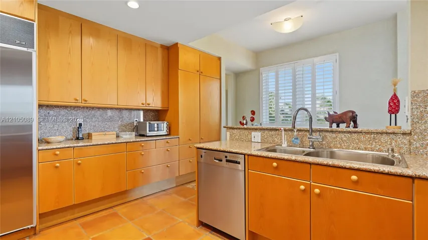Kitchen featuring light wood cabinetry, stone-surface countertops, tile flooring, stainless steel refrigerator and dishwasher, and a double-basin undermount sink with a gooseneck faucet
