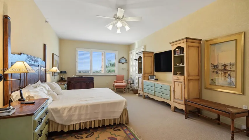 Spacious room featuring neutral carpeting, triple-pane windows with white plantation shutters, and a ceiling-mounted light fixture with a fan
