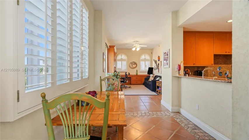 Ceramic tile flooring, white plantation shutters, built-in wooden cabinetry, stone-surfaced breakfast bar, and arched window detailing