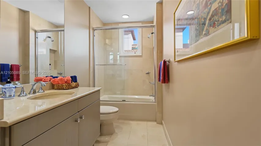 Bathroom featuring a vanity with a light-toned countertop, integrated basin, recessed lighting, and a bathtub with a glass enclosure and wall-tiled surround