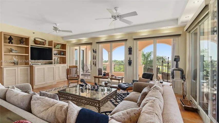 Spacious living area featuring custom built-in cabinetry, tray ceilings with dual overhead fans, recessed lighting, and expansive multi-panel sliding glass doors