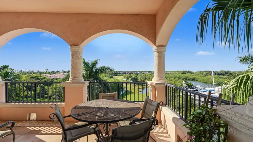 Covered terrace featuring arched stucco openings, decorative stone columns, and metal railings overlooking a waterway and landscape